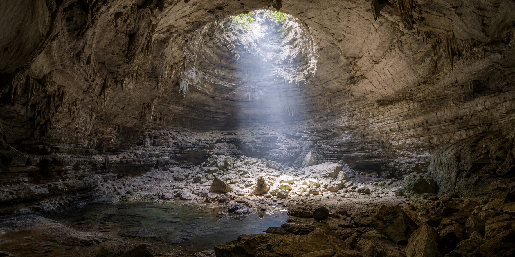 A cave chamber lit through one ceiling opening, the aperture controlling how much reaches in, like a page reproduce setting